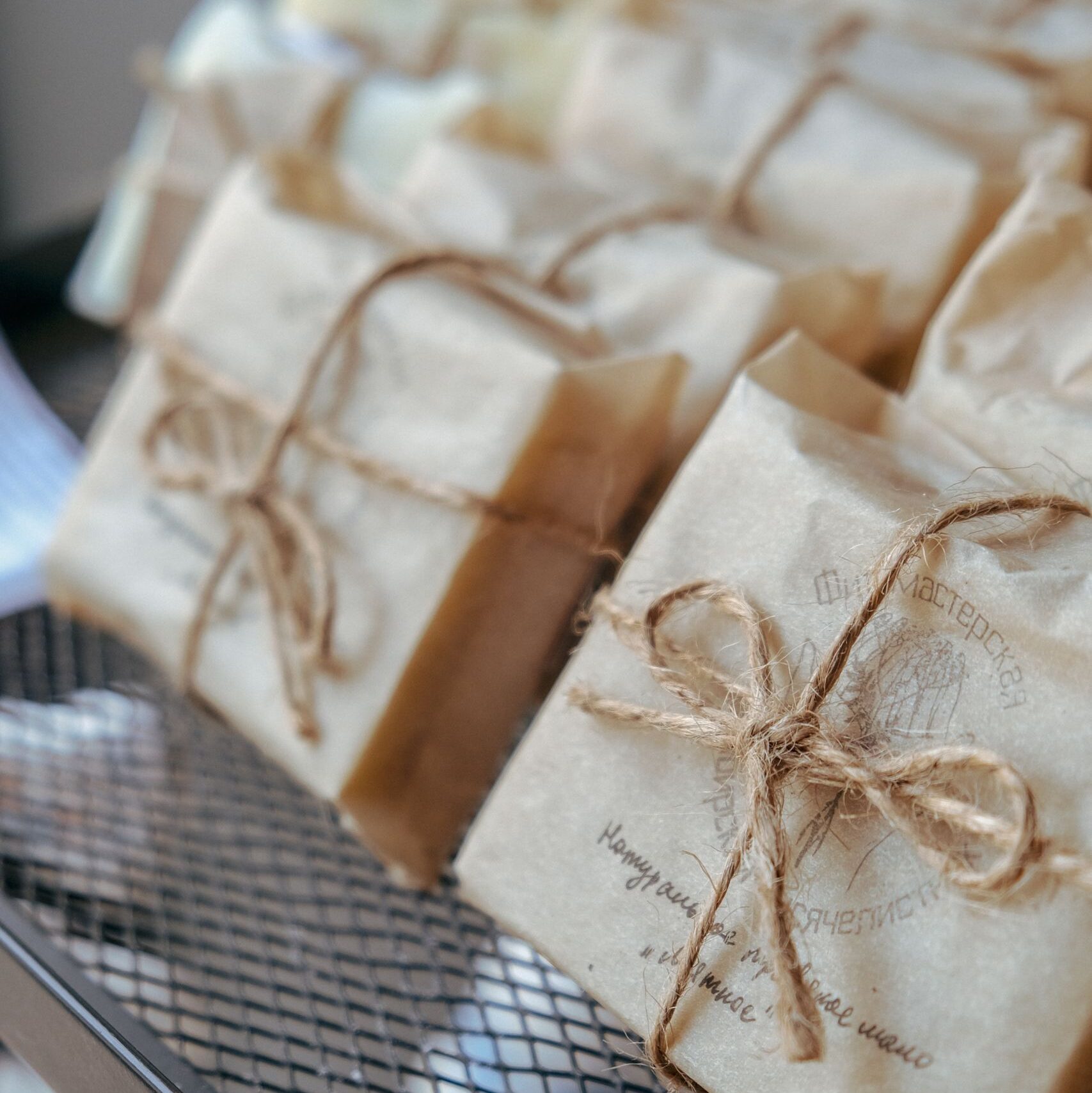 Close-up of handmade soaps wrapped in eco-friendly paper with twine, on a metal rack.