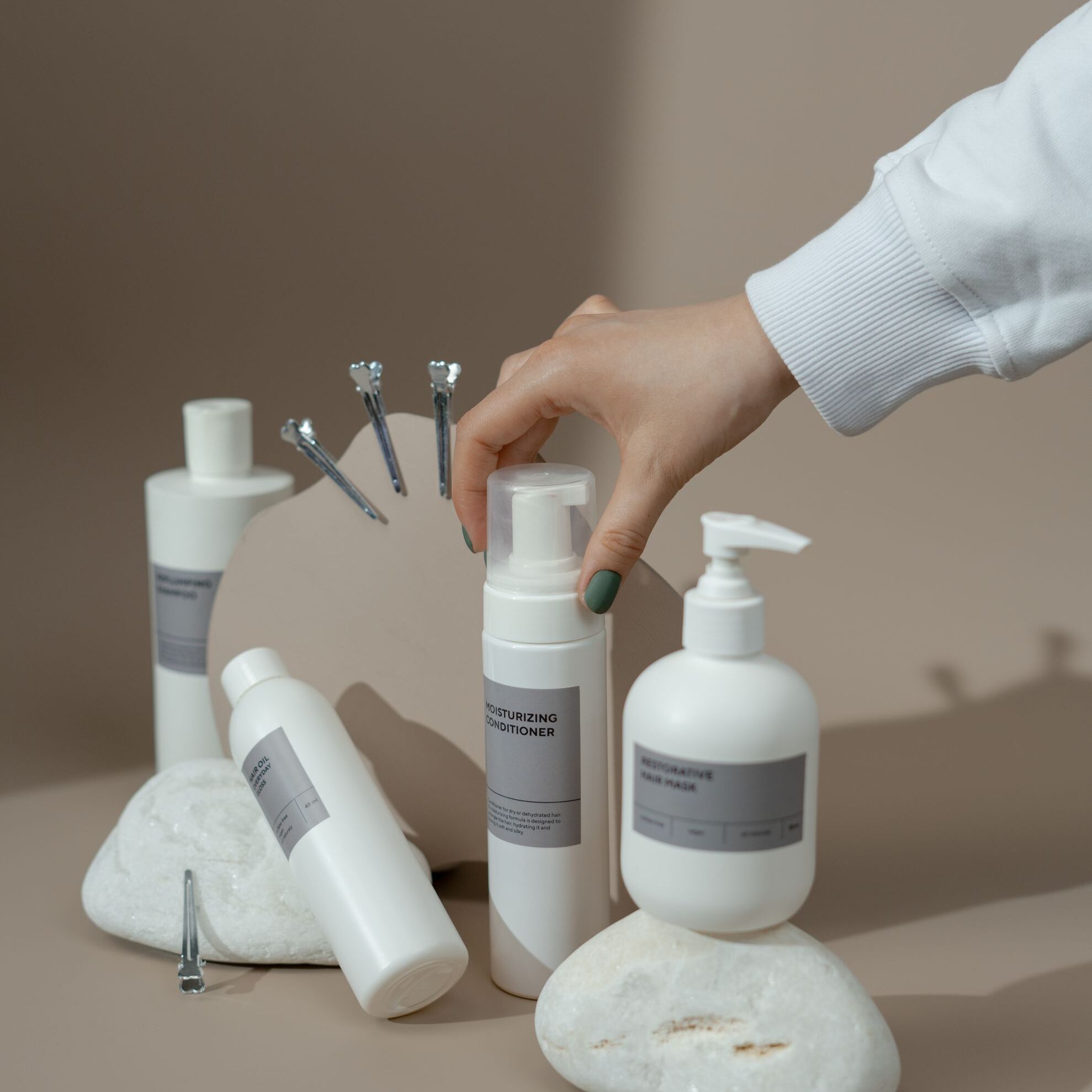 Elegant display of skincare bottles with a hand reaching for one, set against a beige backdrop.