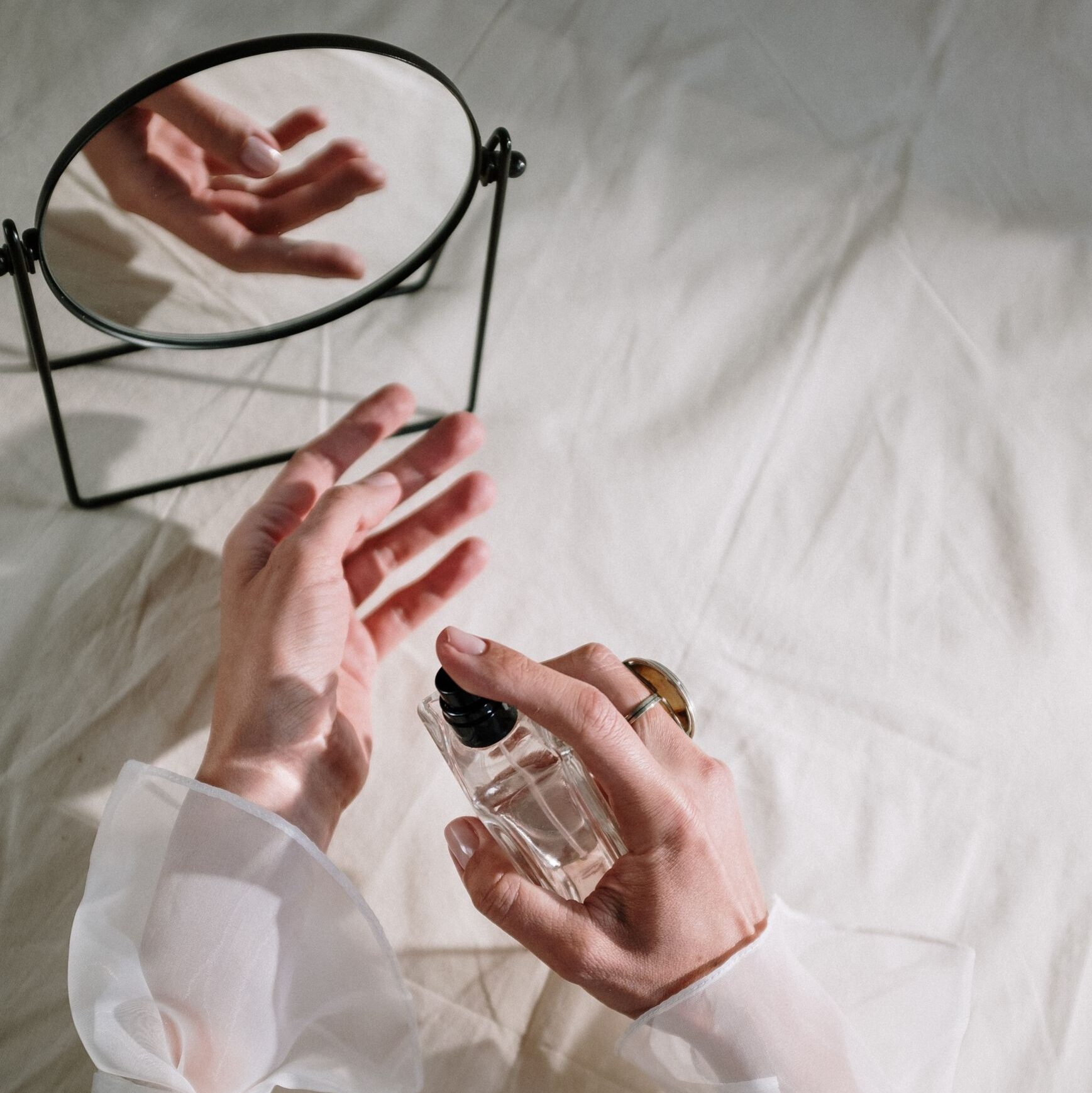 Hands in elegant sheer fabric holding perfume bottle near mirror, creating a graceful reflection.